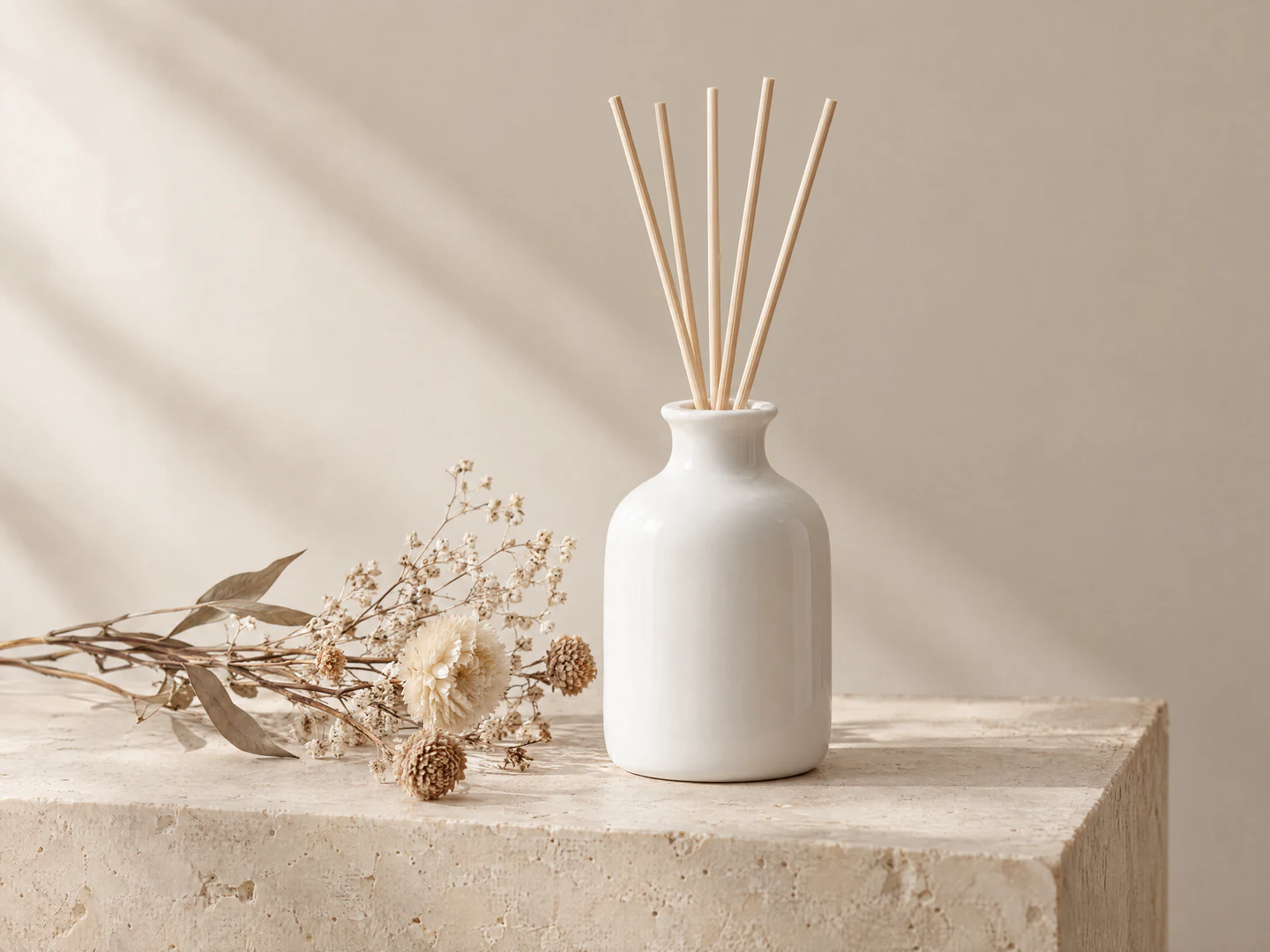 Photo de produit générée par IA d’un diffuseur à bâtonnets en céramique blanche et de fleurs séchées sur un bloc de pierre beige, avec une lumière latérale douce projetant des ombres sur le mur